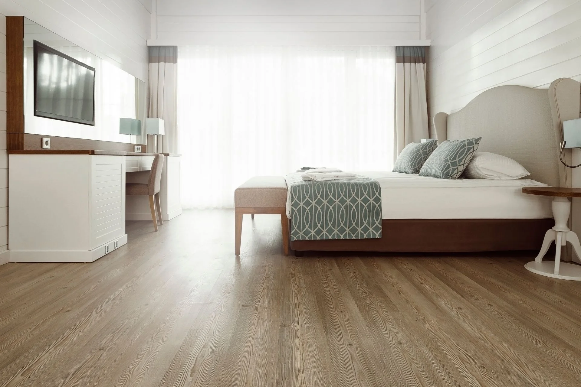 A bedroom with hardwood flooring and a white bed.