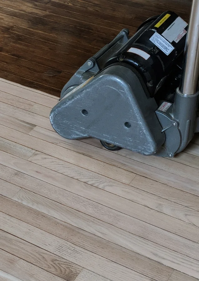 A sander is being used to sand a hardwood floor during refinishing.