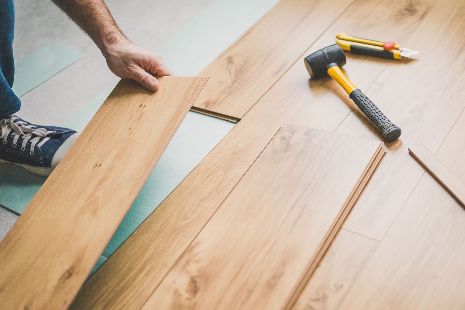 A man is installing hardwood flooring with a hammer.