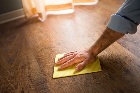 A man polishing hardwood flooring with a yellow cloth.