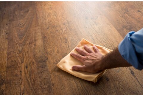 Blog 1 A man performing hardwood flooring maintenance by cleaning a wooden floor with a cloth.