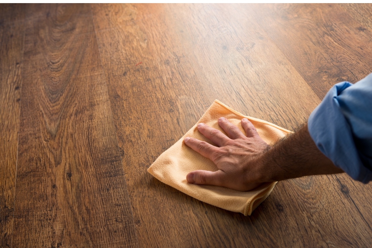 A man performing hardwood flooring maintenance by cleaning a wooden floor with a cloth.