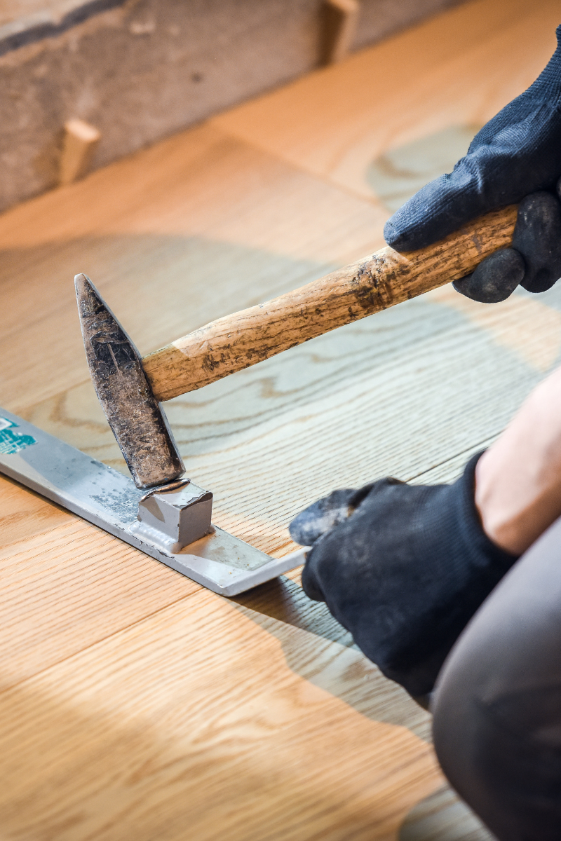 A person is laying wooden flooring using a hammer.