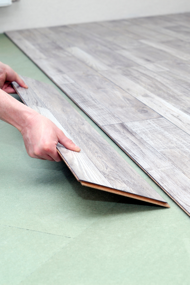 A person is installing a wooden floor from Cumming Flooring Company in a room.