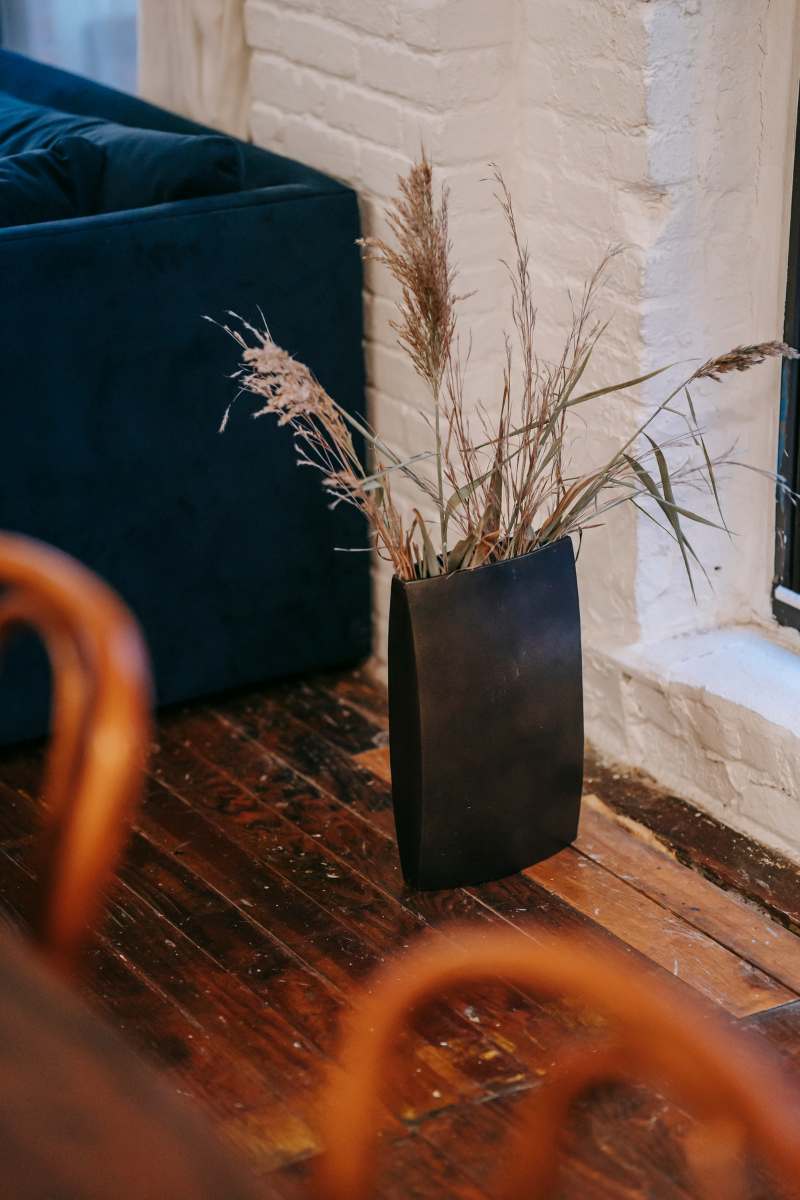 A wooden floor displaying a black vase with a plant, courtesy of Dallas Flooring Company.