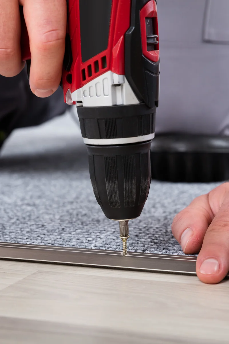 A person using a drill to install carpet.
