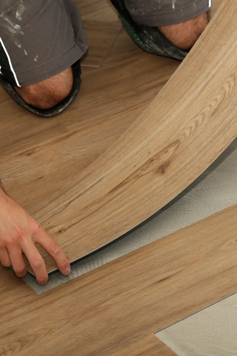 A man is laying down laminate wood flooring for Decatur Flooring Company.
