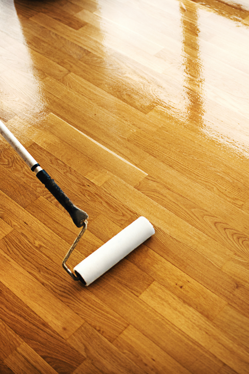 A person is staining a wooden floor with a roller for the Douglasville Flooring Company.