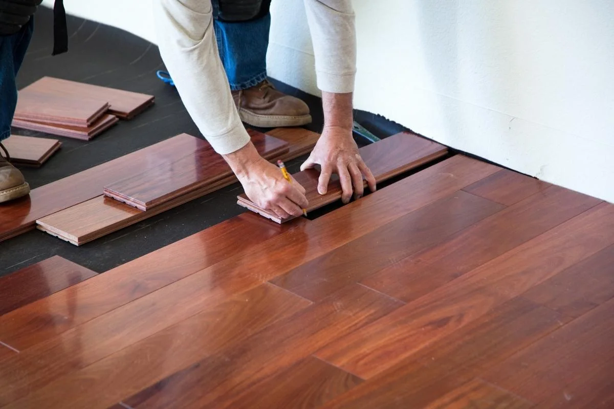 A man installing hardwood flooring in a room.
