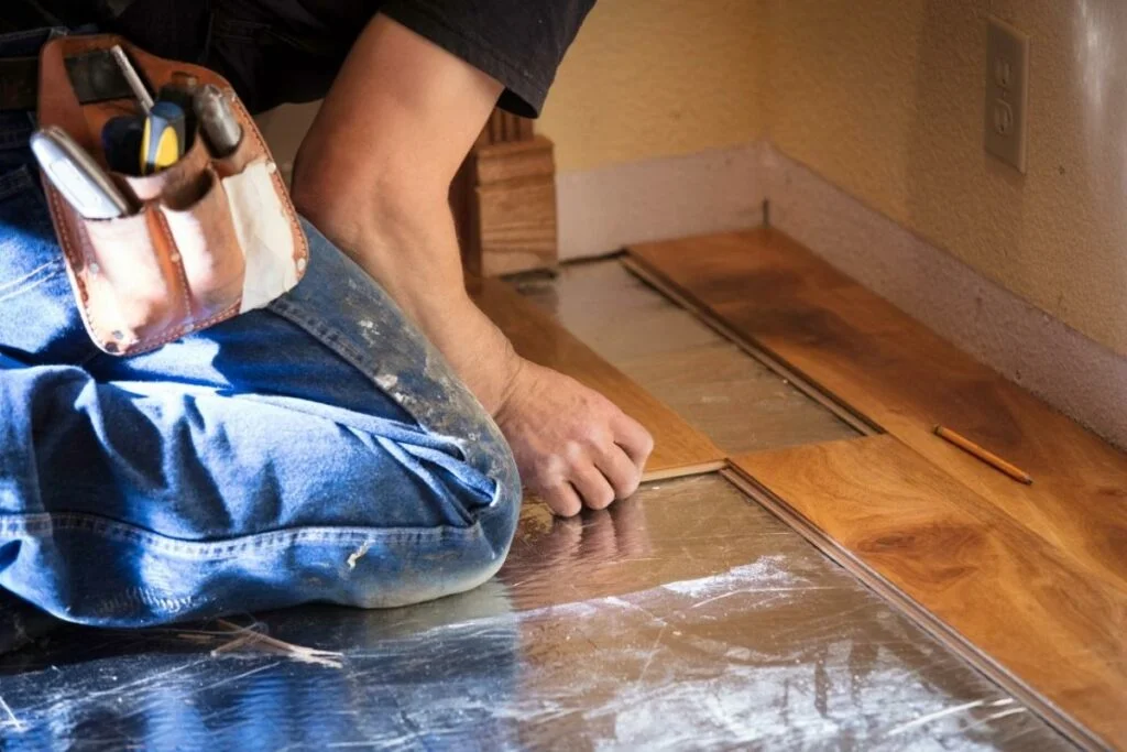 A man is measuring and installing hardwood flooring.
