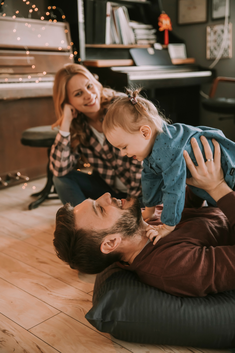 A family is playing with a baby on the floor in front of a piano.