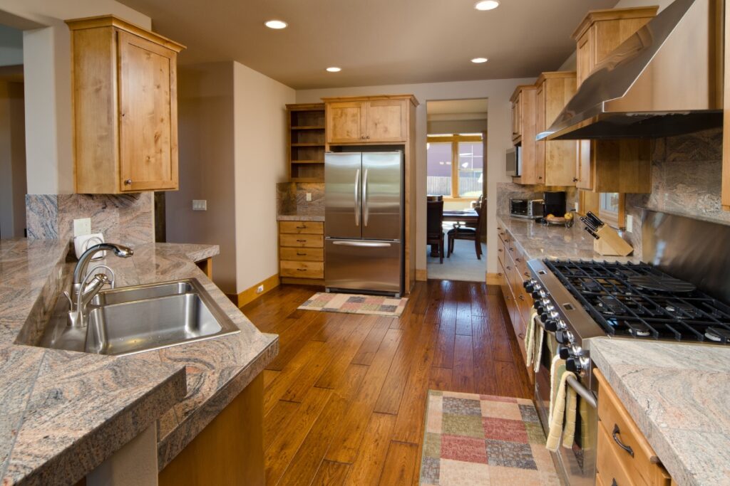 The Pros and Cons of Hardwood Flooring in Kitchens 8 A kitchen with wooden cabinets and granite counter tops, featuring hardwood flooring.