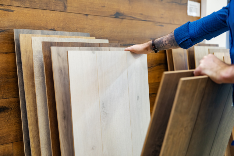 A man is holding a sheet of wood flooring.