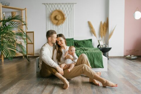 Stylish young family with a baby are sitting on the bedroom floor and enjoying happy moments on hypoallergenic flooring.