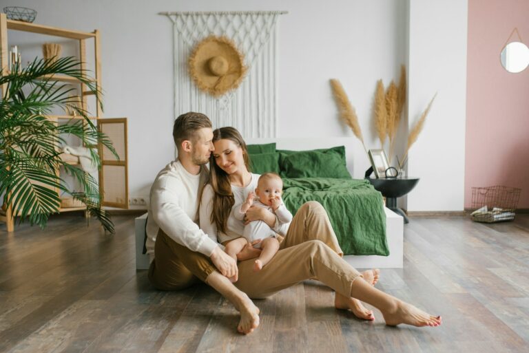 Stylish young family with a baby are sitting on the bedroom floor and enjoying happy moments on hypoallergenic flooring.
