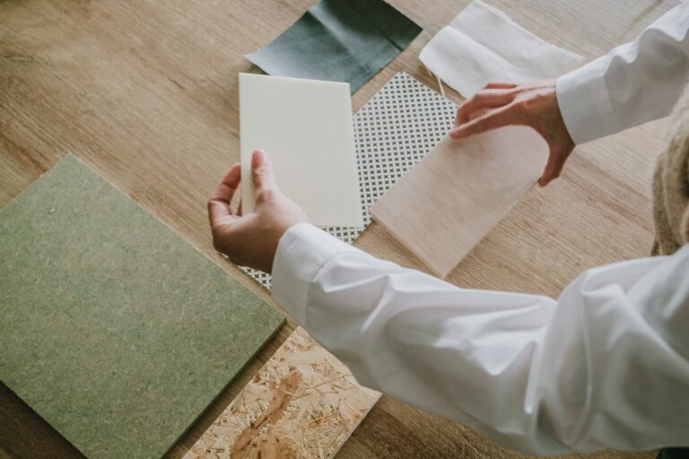 Person in a white shirt handling various fabric and material samples on a wooden surface, perhaps gathering inspiration for sustainable flooring options or green home tips.