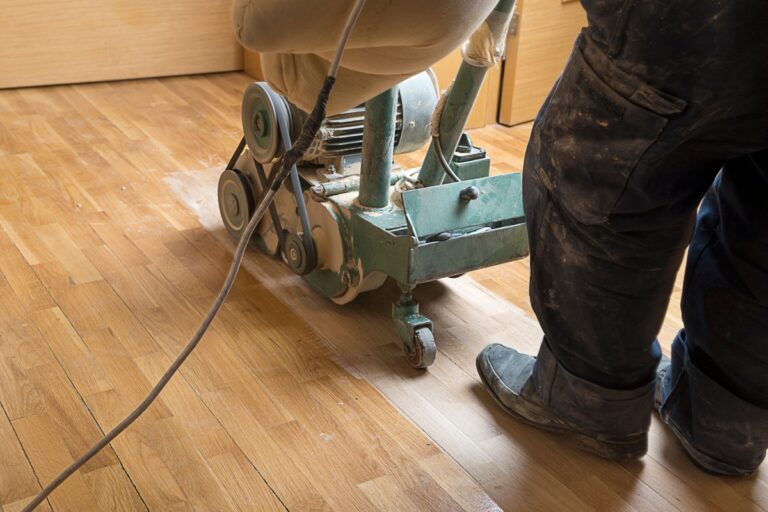 A person expertly operates a floor sanding machine, rejuvenating the wooden surface with precision. As part of essential flooring maintenance tips, regular sanding ensures your floors remain smooth and gleaming.