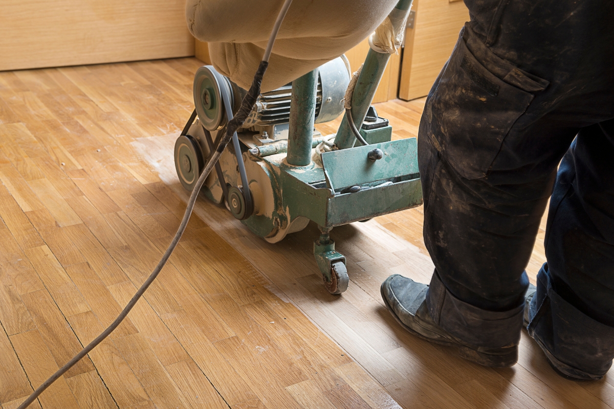 Blog 1 A person expertly operates a floor sanding machine, rejuvenating the wooden surface with precision. As part of essential flooring maintenance tips, regular sanding ensures your floors remain smooth and gleaming.