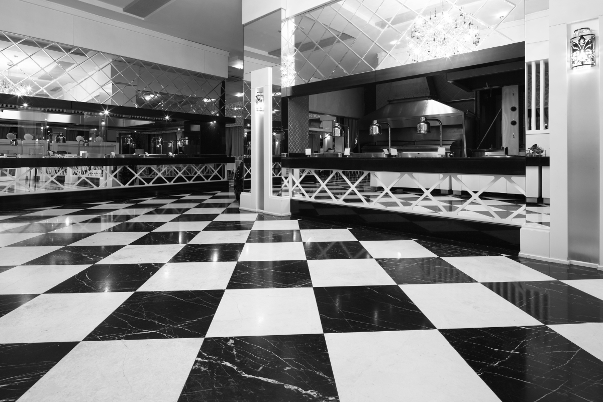 Luxury Home Flooring Ideas for Buckhead: Hardwood, Tile, and More 2 A black-and-white photo of a restaurant interior featuring luxury home flooring in a checkered tile pattern, mirrored walls, and a visible kitchen area in the background.