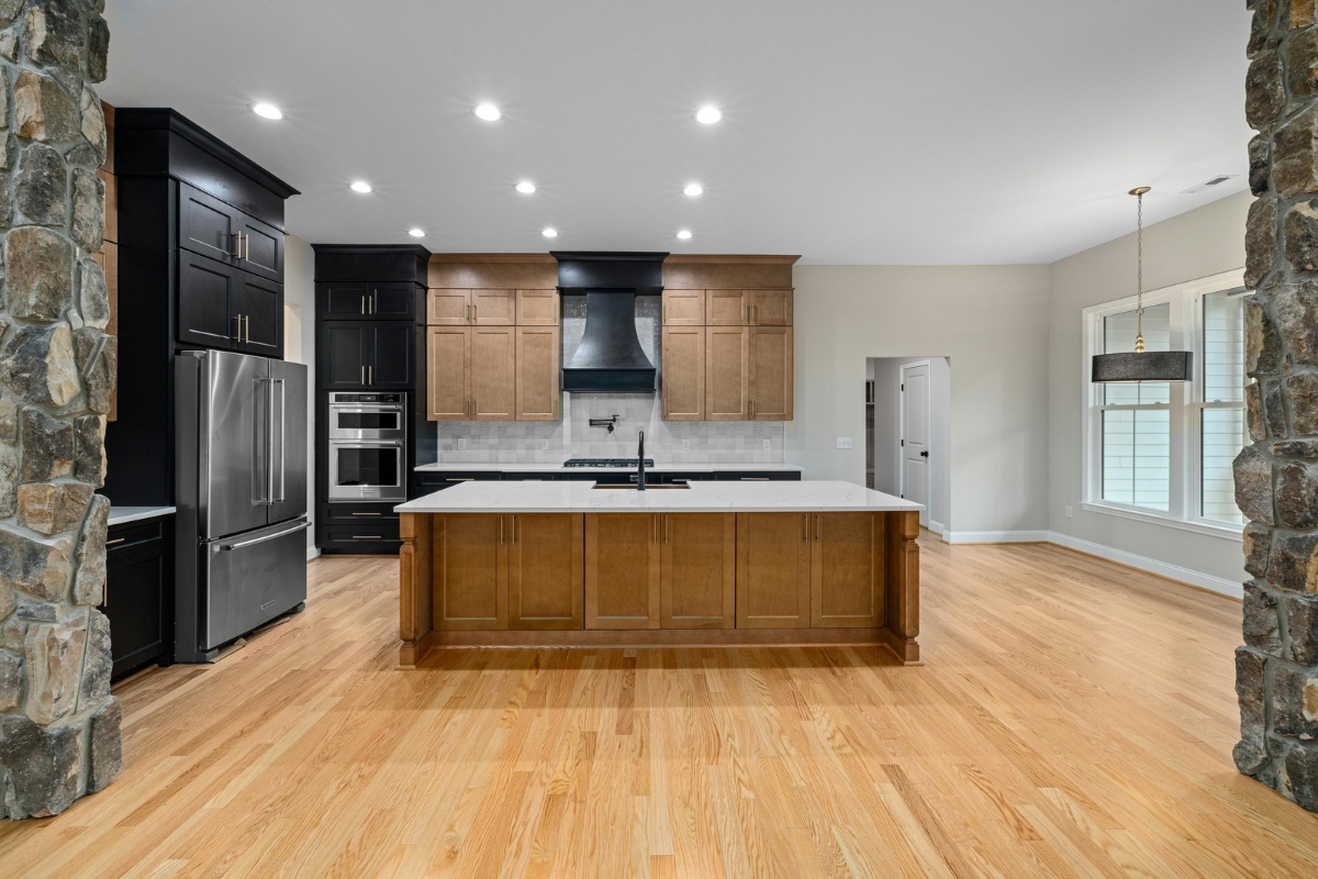 Luxury Home Flooring Ideas for Buckhead: Hardwood, Tile, and More 1 Modern kitchen with luxury home flooring, black and wood cabinets, stainless steel appliances, a large island with sink, and stone pillars elegantly framing the space.