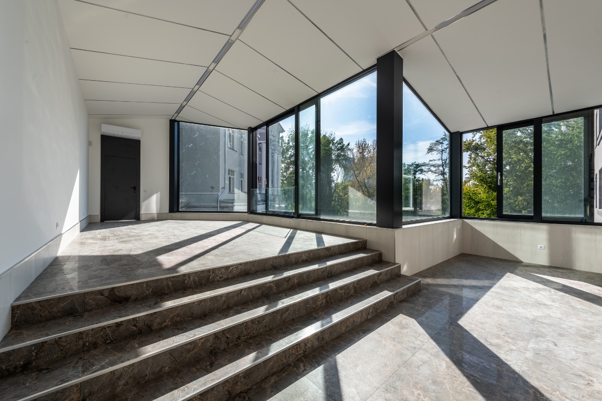 Luxury Home Flooring Ideas for Buckhead: Hardwood, Tile, and More 5 Spacious modern room with luxury home flooring, marble steps, large floor-to-ceiling windows, and a view of trees and buildings outside.