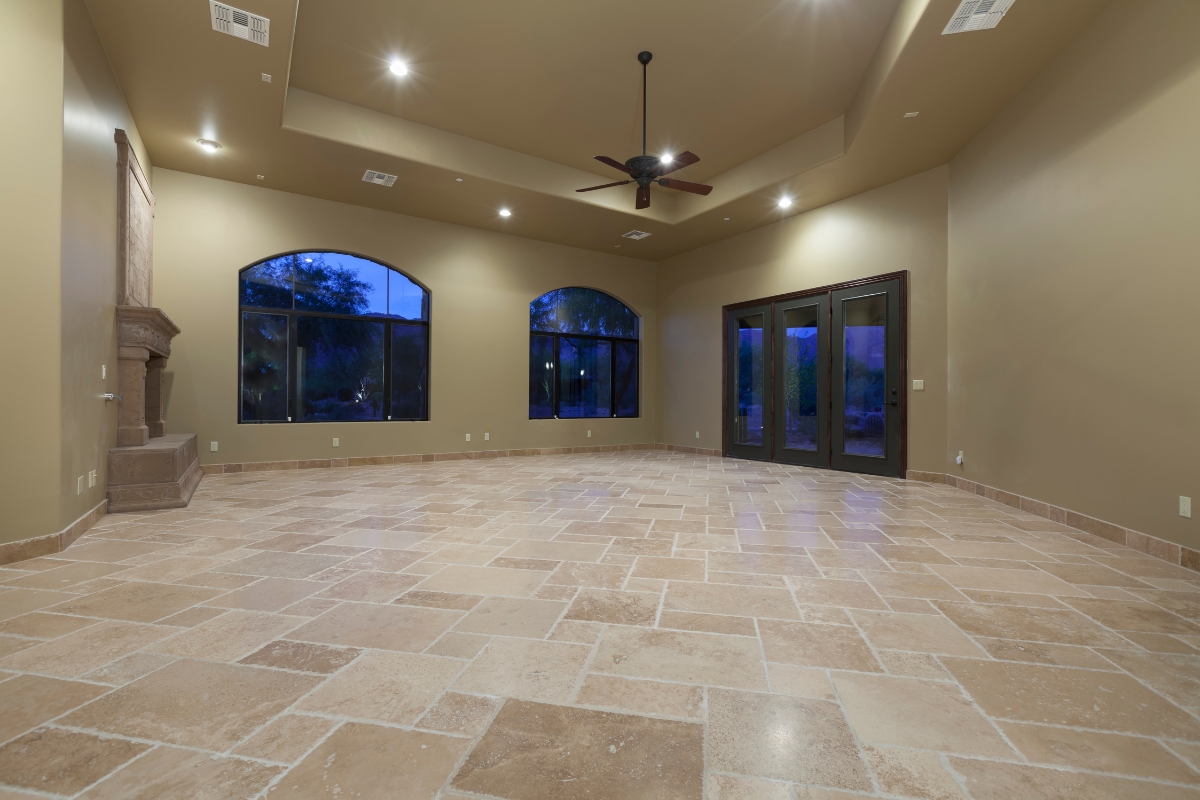 Luxury Home Flooring Ideas for Buckhead: Hardwood, Tile, and More 8 Spacious, empty room with luxury home flooring in beige tile, tan walls, large arched windows, a ceiling fan, and double glass doors leading outside.