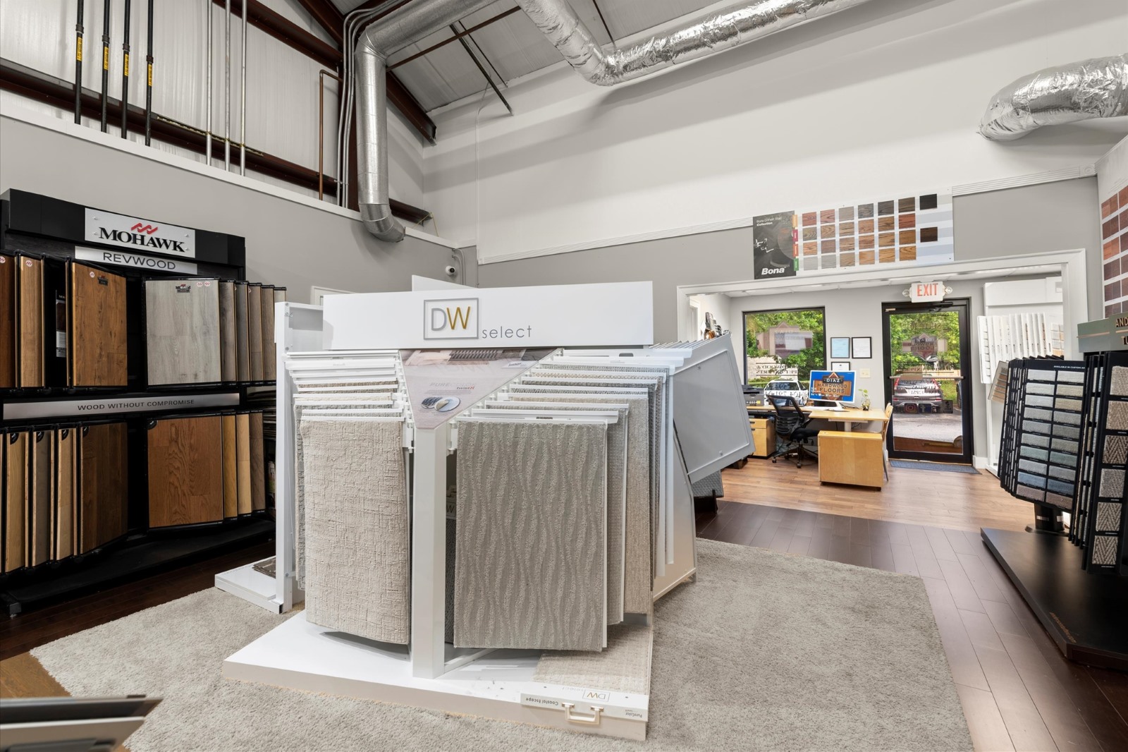 A showroom displays carpet and flooring samples on racks, with an office area in the background and sample boards on the walls—perfect for planning your next carpet installation.