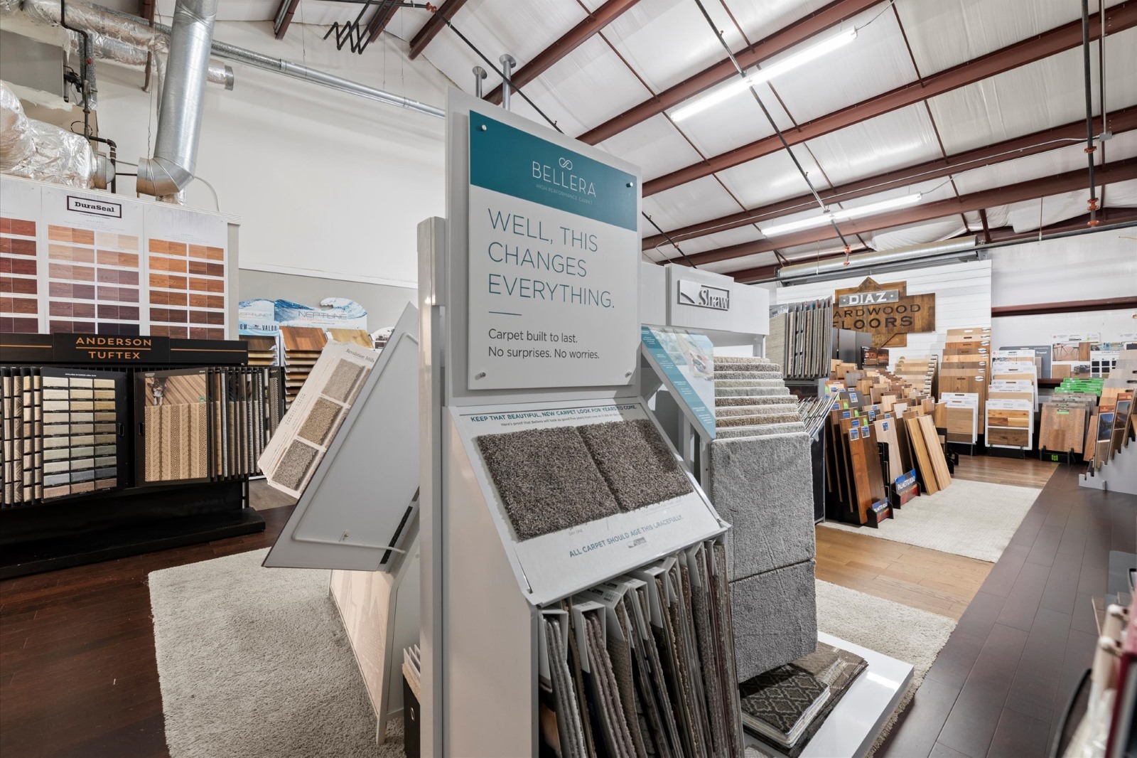 Learn about a flooring store interior displaying carpet and wood flooring samples on racks beneath high ceilings with exposed beams and ducts.