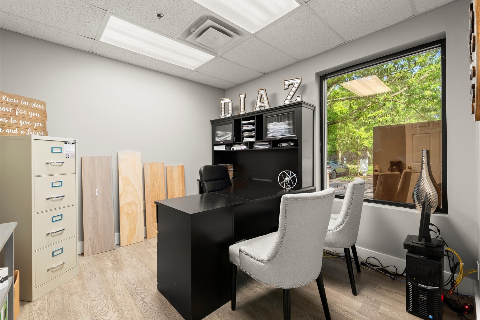 Modern office with a black desk, two white chairs, filing cabinet, wood samples, and a window showing green trees outside. The name "DIAZ" is displayed on a shelf above the desk, highlighting the company’s service areas.