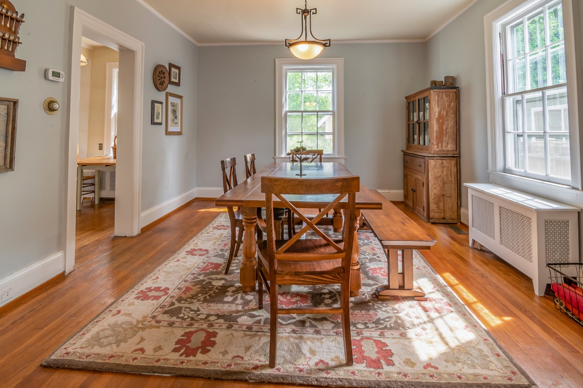 Scratch-Resistant Hardwood Floors for Cartersville Homes: Tips to Prevent Damage 5 A dining room with a wooden table, chairs, a bench, area rug, sideboard, and large windows letting in natural light sits atop scratch-resistant hardwood floors.