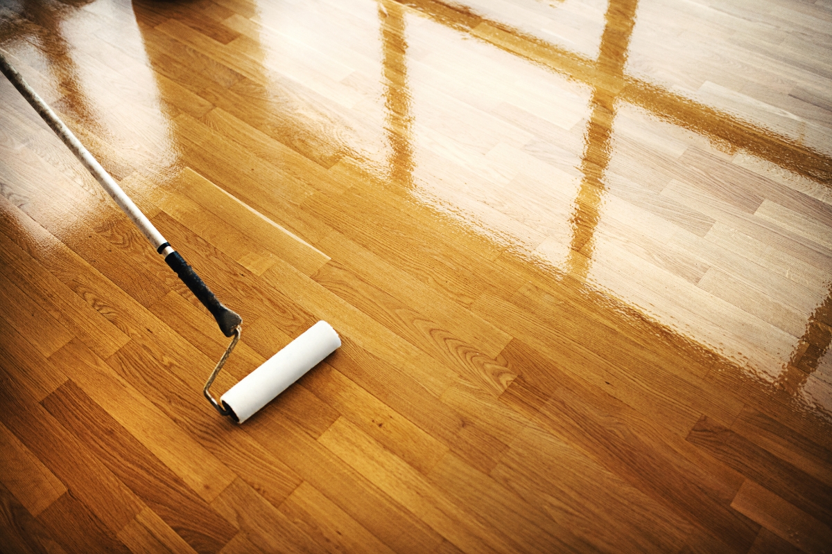Scratch-Resistant Hardwood Floors for Cartersville Homes: Tips to Prevent Damage 1 A paint roller is being used to apply a finish to a wooden floor, with part of the scratch-resistant hardwood floor visibly coated and shiny.