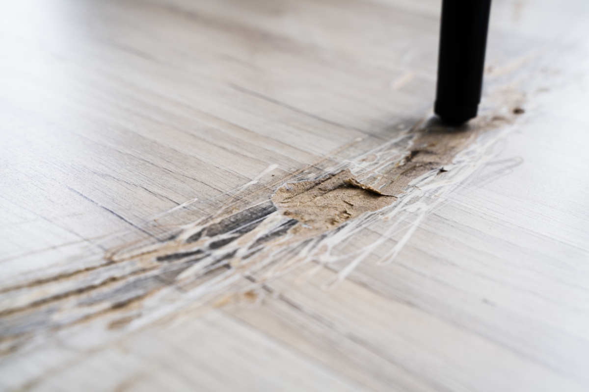 Wood Floor Refinishing in Brookhaven: Key Signs It's Time to Refinish Your Floors 2 Close-up of a wood floor with visible deep scratches and damage, caused by the leg of a piece of furniture dragging across the surface.