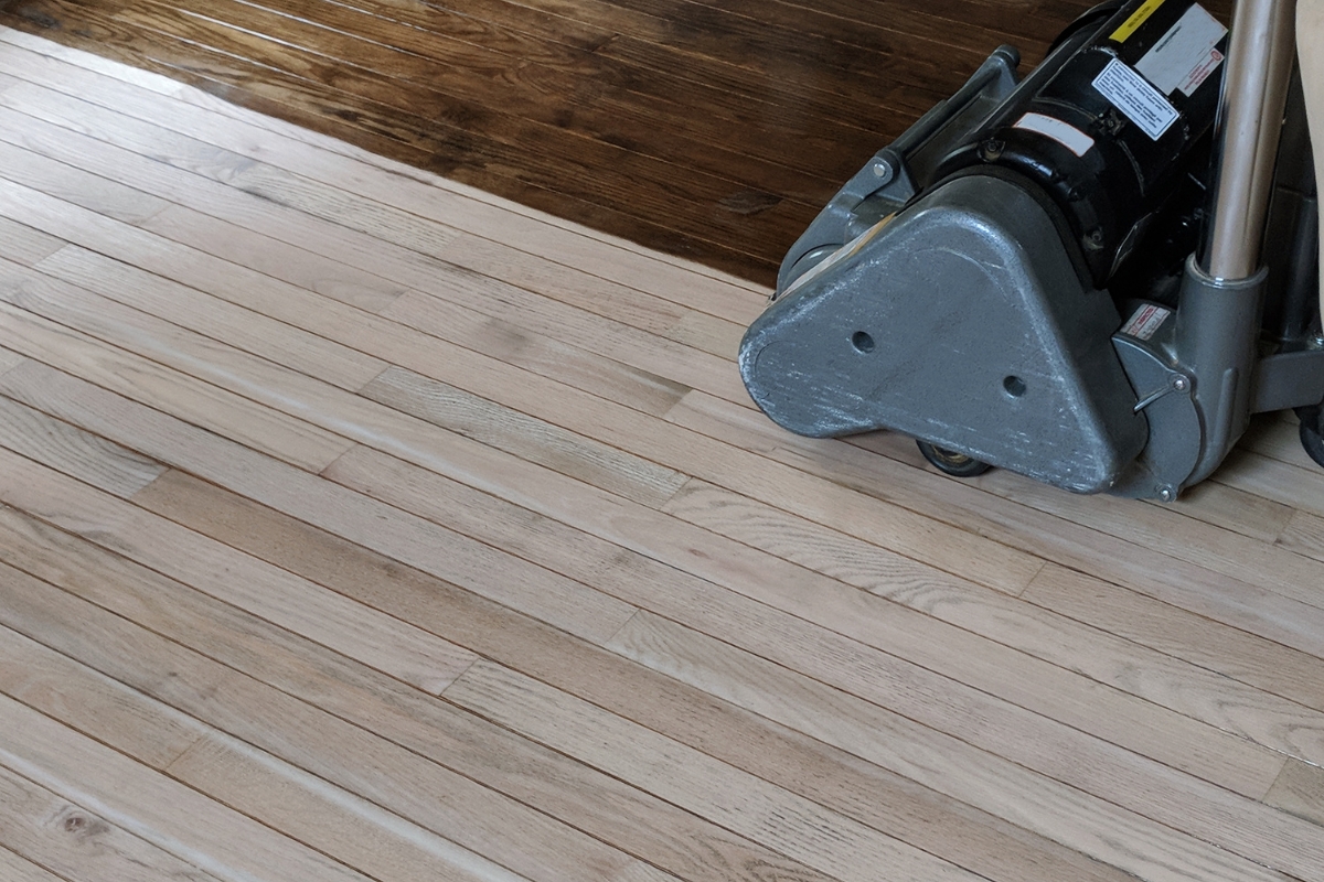 Wood Floor Refinishing in Brookhaven: Key Signs It's Time to Refinish Your Floors 4 A floor sander is being used on a wood floor, highlighting the striking contrast between the unfinished light wood and the finished dark-stained wood.