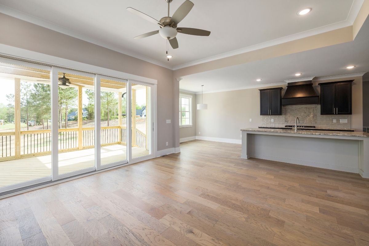 Wood Floor Refinishing in Brookhaven: Key Signs It's Time to Refinish Your Floors 7 A spacious empty living area features a striking wood floor, ceiling fan, large sliding glass doors, and a modern kitchen with dark cabinets and a breakfast bar.