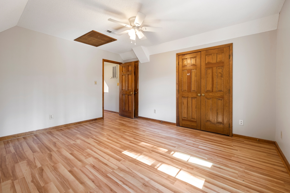 Wood Floor Refinishing in Brookhaven: Key Signs It's Time to Refinish Your Floors 8 Empty room with a beautiful wood floor, white walls, ceiling fan, two wooden doors, and sunlight streaming through a window.
