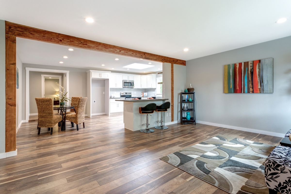 Wood Floor Finish Guide for Canton Homeowners 5 Open-plan living area featuring a stylish wood floor finish, a small dining table, modern kitchen with bar stools, and abstract wall art above a rug.
