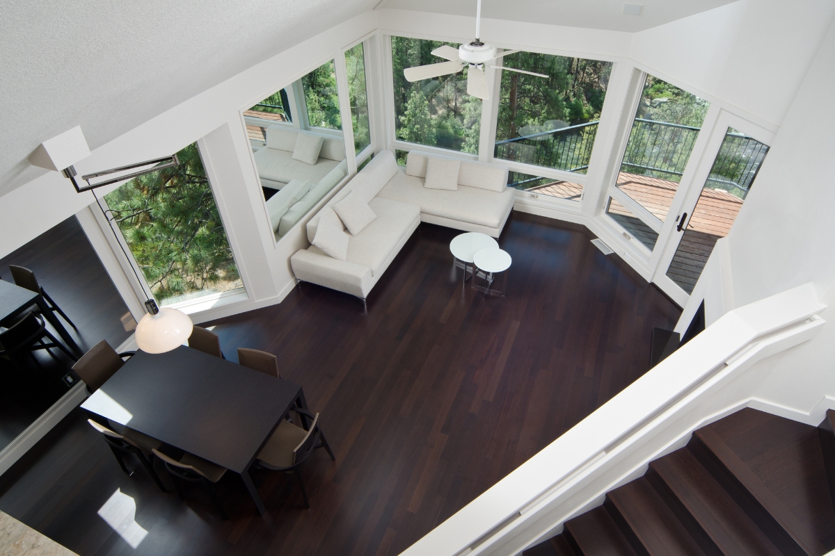 Best Flooring Options for High-Traffic Areas in Chamblee Homes 1 A modern living and dining area featuring dark wood floors—one of the best flooring options—white sectional sofa, round tables, large windows, and a ceiling fan, all viewed from an upstairs angle.