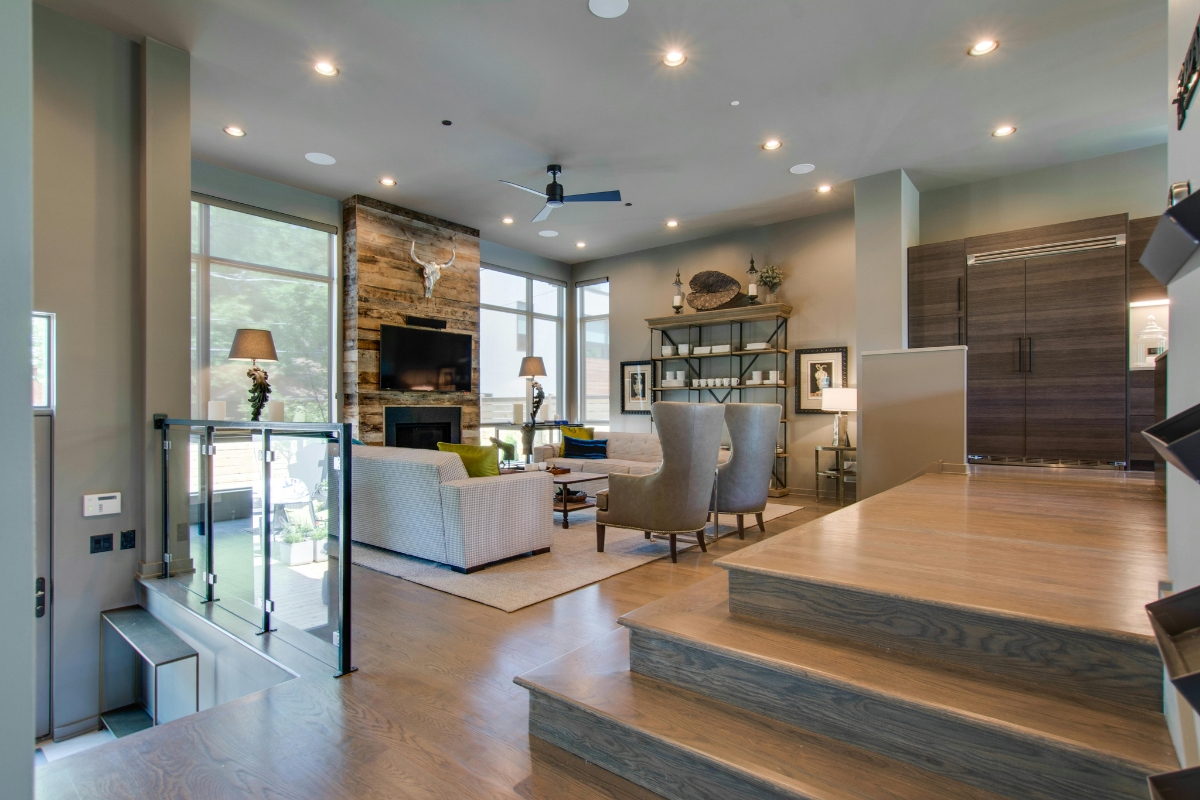 Modern living room with one of the best flooring options—wood floors—neutral-toned furniture, a fireplace with a stone accent wall, large windows, and recessed lighting.