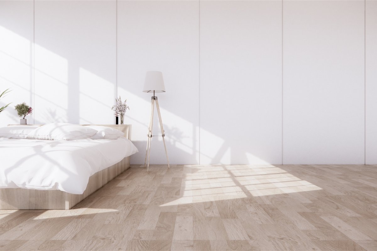 Waterproof Flooring Options for Cumming Homes: What You Need to Know 14 Minimalist bedroom with a low wooden bed, white bedding, potted plants, a standing lamp, and sunlight streaming onto waterproof flooring—a stylish choice often featured in Cumming homes.