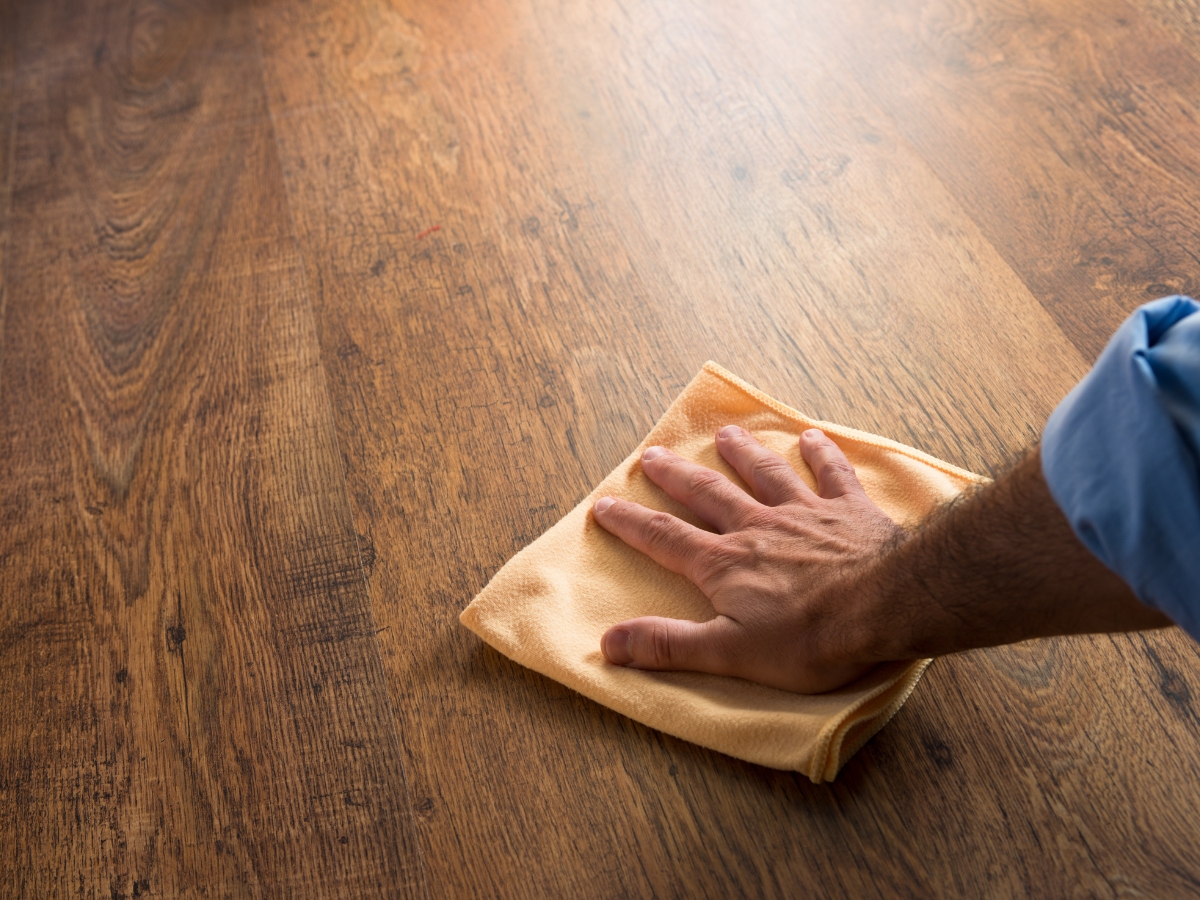 How to Restore Hardwood Floors in Older Decatur Homes Without Damaging Them 10 A person’s hand wipes a wooden surface with a beige cloth to help restore hardwood floors.