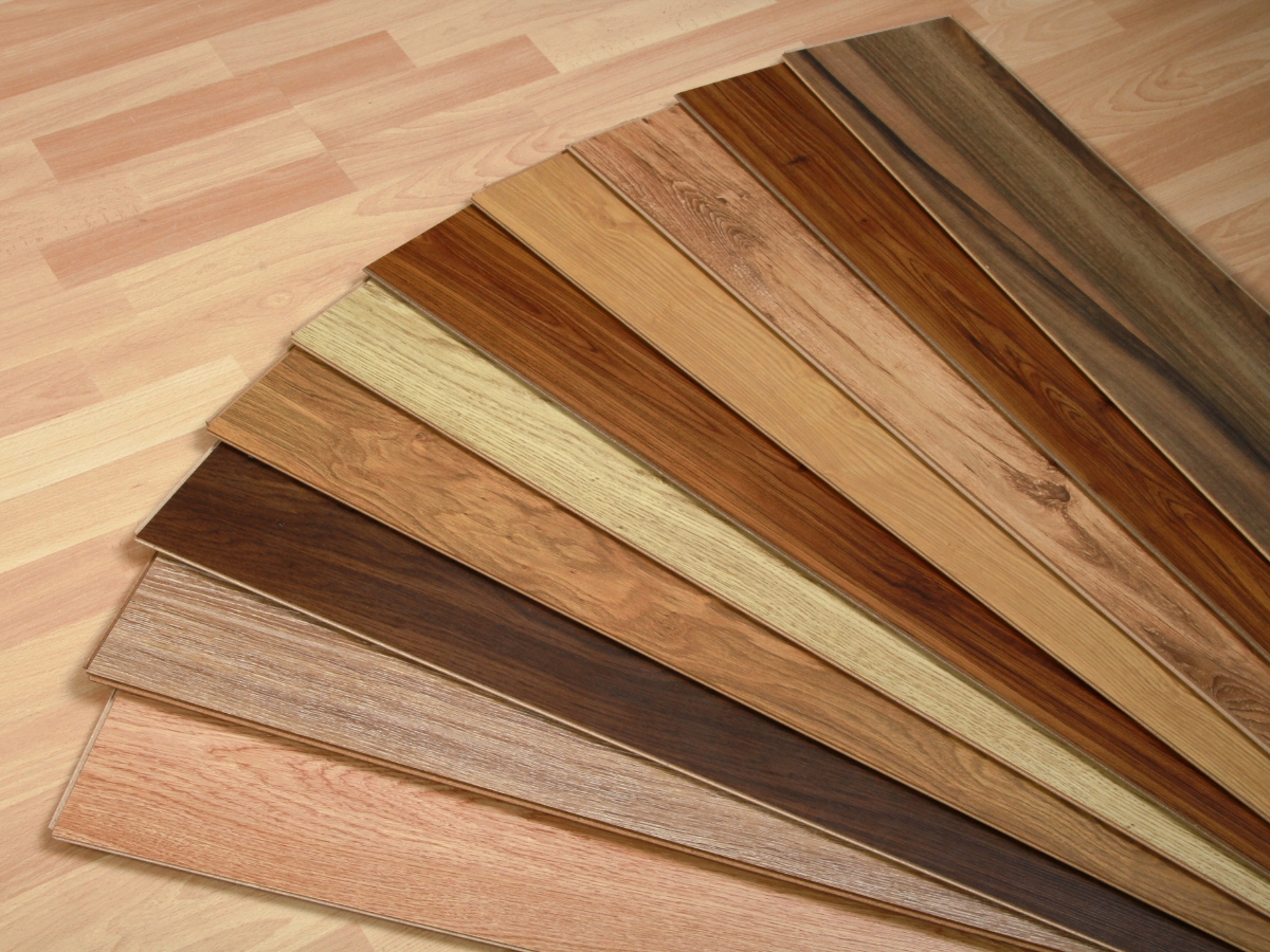 Johns Creek Home Flooring Guide: Hardwood, Laminate, or Vinyl? 4 Several wooden flooring planks in different shades and wood grains are arranged in a fan shape on a light wood floor background, offering inspiration for your next project with the Johns Creek Home Flooring Guide.