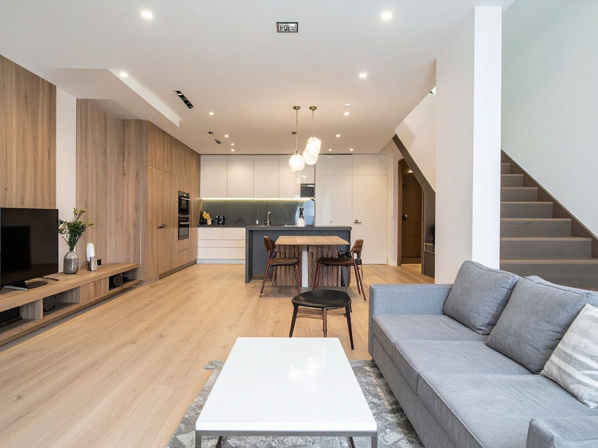 Top Flooring Options for Open-Concept Homes in Lithia Springs, GA 2 Modern open-plan living area with light wood floors, a gray sofa, white coffee table, kitchen with island, and wooden staircase—showcasing one of the top flooring options for open-concept homes in Lithia Springs.