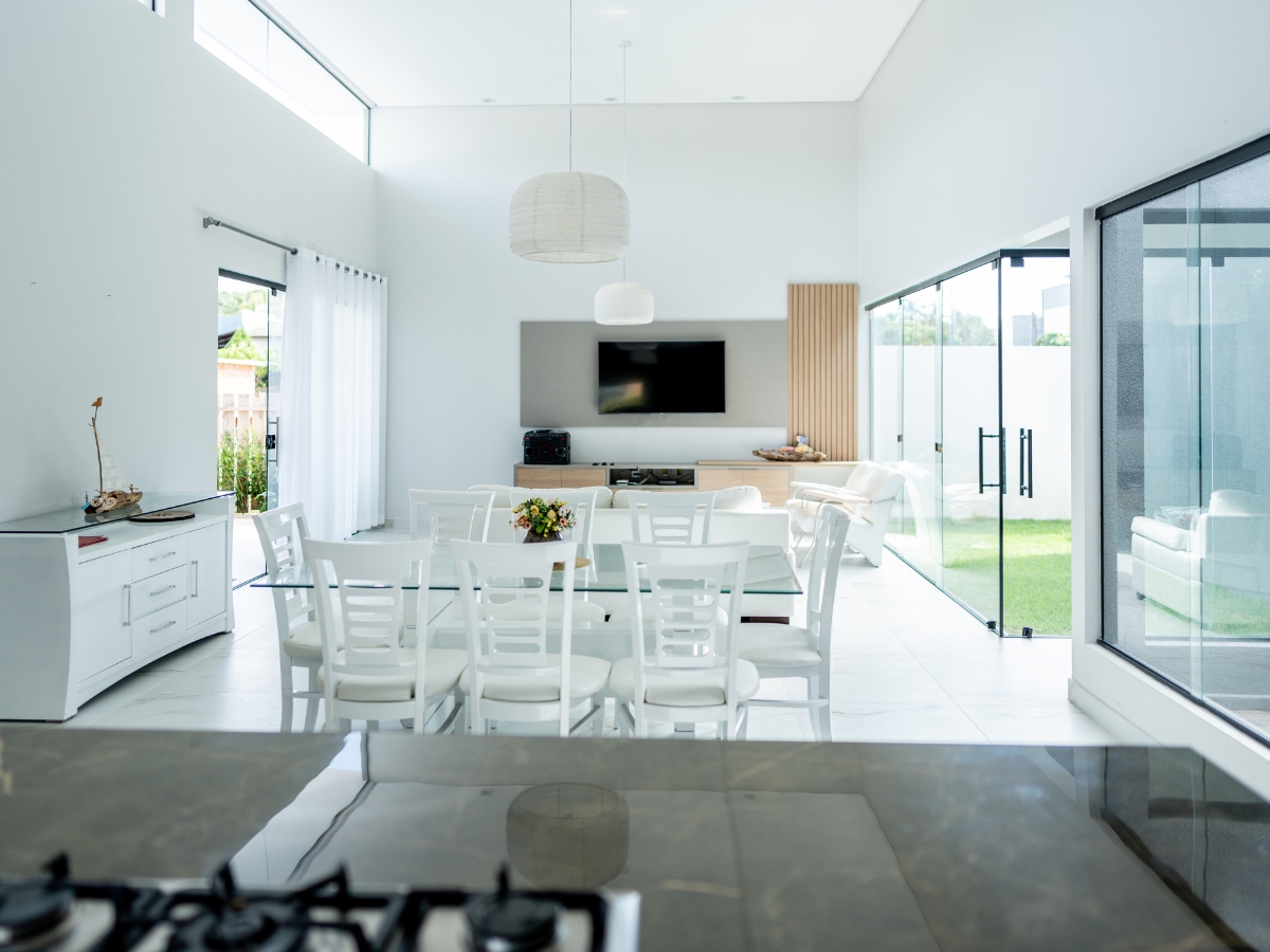 Top Flooring Options for Open-Concept Homes in Lithia Springs, GA 3 Modern open-plan living and dining area with white furniture, large windows, and a wall-mounted TV showcases one of the top flooring options for open-concept homes in Lithia Springs, enhanced by sliding glass doors opening to a lush green outdoor space.