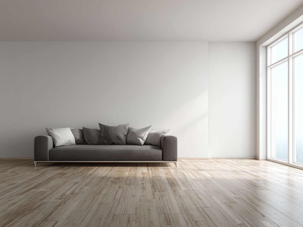 A modern living room with a gray sofa, several throw pillows, light wood flooring, a large window, and white walls creates the perfect setting for your Acclimation Guide.