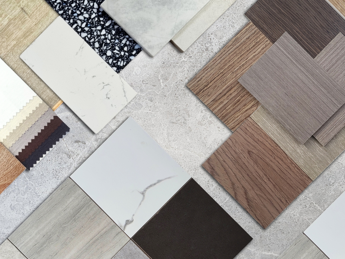 Assorted samples of wood, stone, and fabric swatches arranged on a gray textured surface, showcasing various colors and patterns ideal for interior design in small spaces.