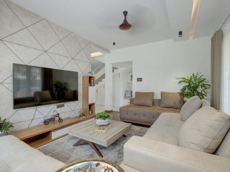 Modern living room designed for small spaces, featuring neutral-toned sofas, a geometric accent wall, flat-screen TV, potted plants, and a wooden coffee table arranged on a gray rug.