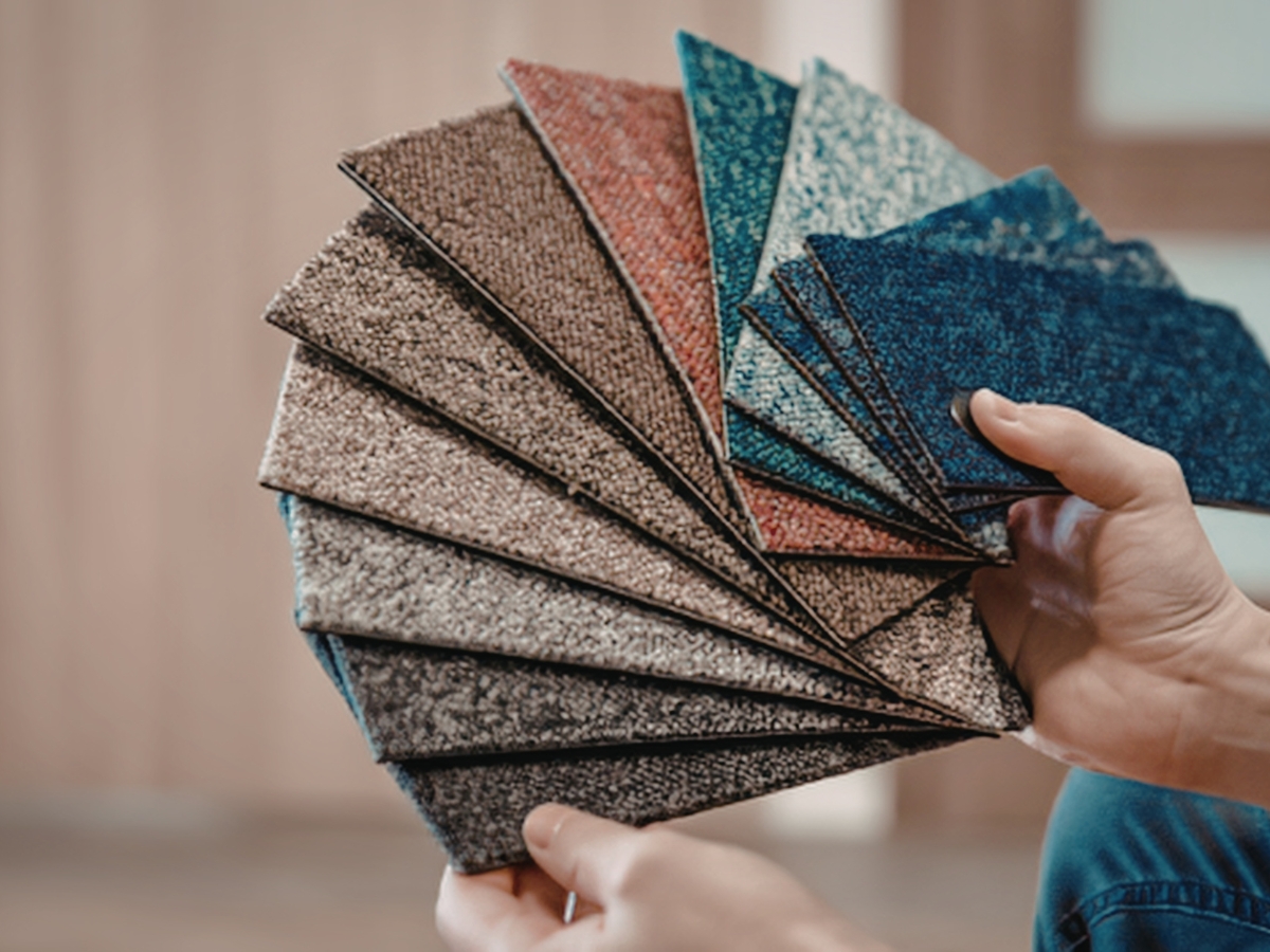 A person holds a fan of carpet samples in various colors and textures, showcasing flooring options and demonstrating expert color matching for any space.