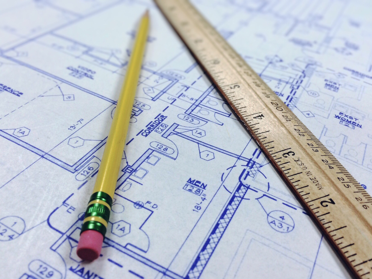 A Room Measurement Guide: Basics for Better Flooring Estimates 3 A yellow pencil and a wooden ruler rest on architectural blueprints, serving as a precise measurement guide for detailed floor plans and room dimensions.