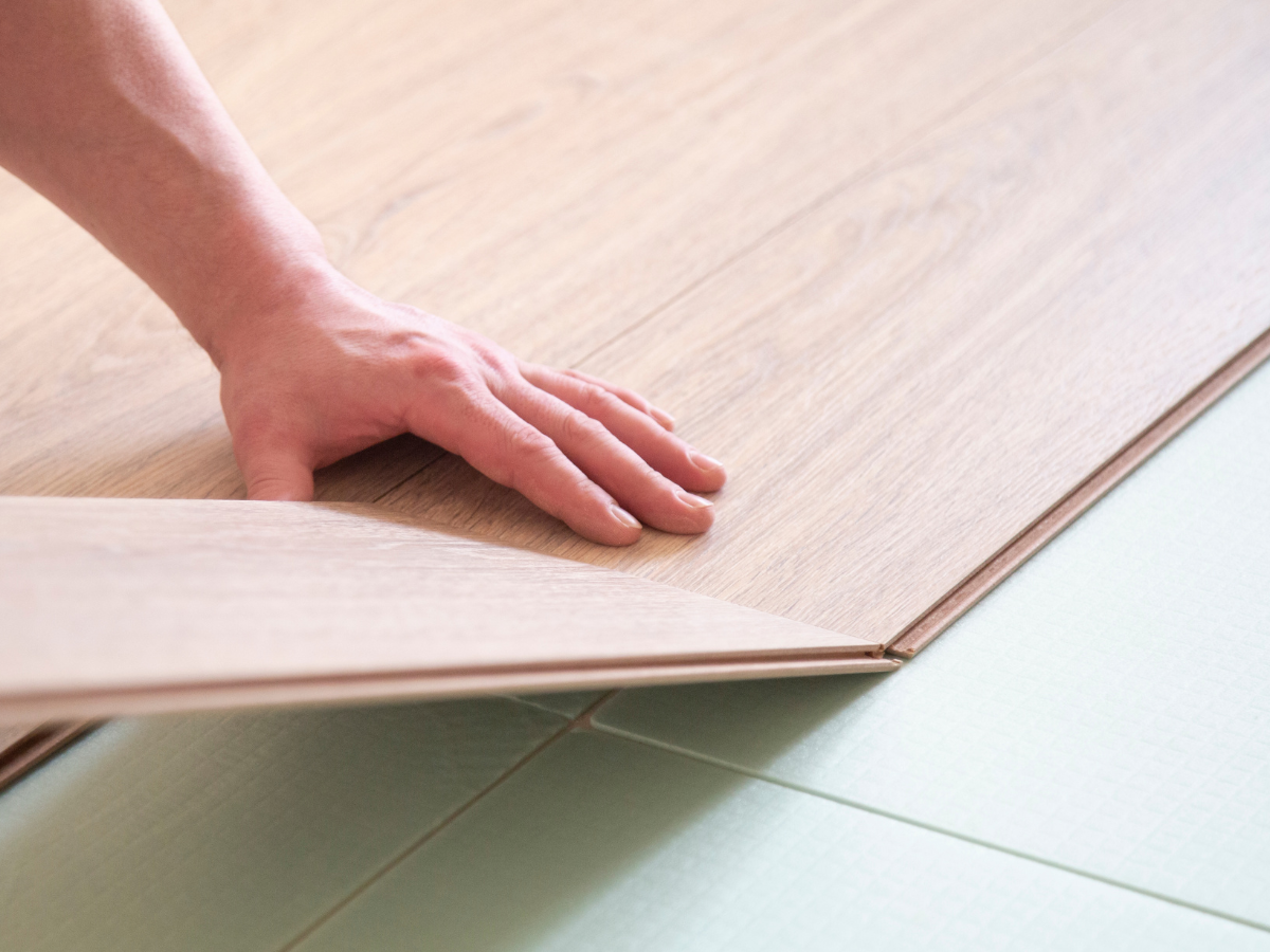 Is Bamboo Flooring Right for You? 8 A person installs a wooden laminate flooring panel by aligning and snapping it into place over a green underlayment, similar to the method used with bamboo flooring for a seamless finish.