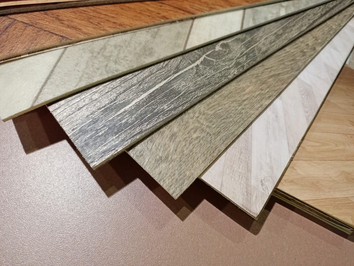Cozy & Stylish Bedroom Flooring Ideas 2 A display of vinyl flooring samples in various wood and stone patterns, fanned out on a brown surface—perfect inspiration for your next bedroom flooring project.